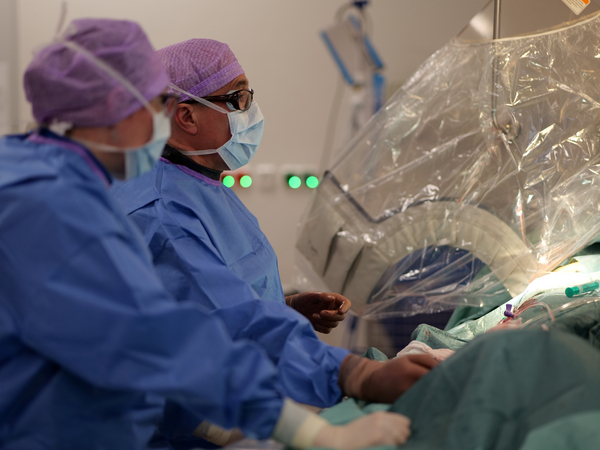 Zwei Operateure mit OP-Kleidung, Kopfhauben und Mundschutz blicken während einer Operation in Richtung des hell erleuchteten Operationsfelds im Albertinen Herz- und Gefäßzentrum am Standort Amalie Sieveking Krankenhaus