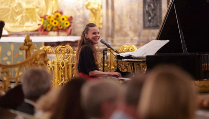 Eine Pianistin sitzt am Konzertflügel und blickt zum Publikum im Kirchensaal beim 10. Herzbrücke-Benefizkonzert im Hamburger „Michel“ der Albertinen-Stiftung.