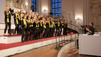 Der Albertinen Mitarbeitenden Gospelchor steht beim Singen auf einer Tribüne im festlichen Kirchensaal beim 10. Herzbrücke-Benefizkonzert im Hamburger „Michel“ der Albertinen-Stiftung.