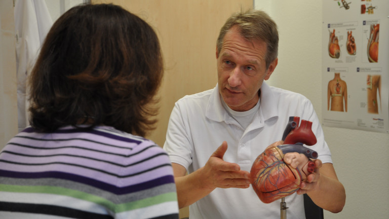 Prof. Dr. Nägele im Gespräch mit einer Patientin an einem Tisch mit einem plastischen Modell eines Herzens im Albertinen Herz- und Gefäßzentrum in Hamburg Prof. Dr. Nägele im Gespräch mit einer Patientin an einem Tisch mit einem plastischen Modell eines Herzens im Albertinen Herz- und Gefäßzentrum in Hamburg