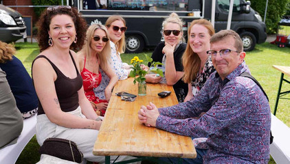 Sechs Mitarbeitende sitzen an einer Bierbank und blicken lachend in die Kamera beim Sommerfest 2026 auf dem Gesundheitscampus Volksdorf des Evangelischen Amalie Sieveking Krankenhauses, der Residenz am Wiesenkamp, des Feierabendhauses Volksdorf und der Albertinen Kindertagesstätte Volksdorf.