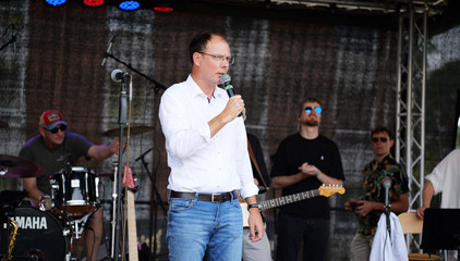 Andreas Schneider, Geschäftsführer im Ev. Amalie Sieveking Krankenhaus, steht auf der Konzertbühne mit einem Mikrofon bei seiner Rede beim Sommerfest 2026 auf dem Gesundheitscampus Volksdorf des Evangelischen Amalie Sieveking Krankenhauses, der Residenz am Wiesenkamp, des Feierabendhauses Volksdorf und der Albertinen Kindertagesstätte Volksdorf. 