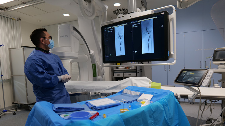 Dr. Ammar Moubayed blickt in OP Kleidung in der Angiosuite auf den Bildschirm mit Befunden einer Angiographie