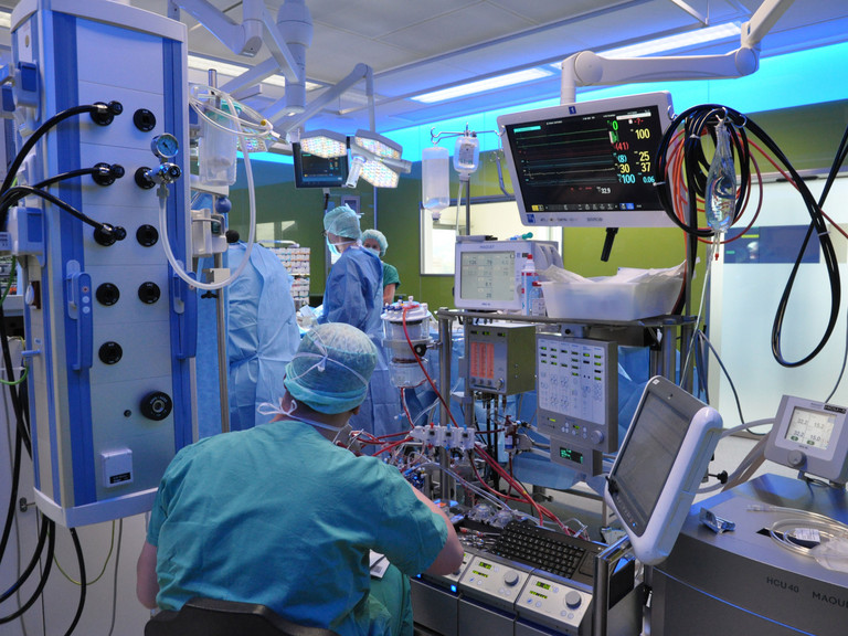 Ein Kardiotechniker sitzt vor einer Reihe medizinischer Gerätschaften mit einem Überwachungsmonitor während einer Operation in einem blau erleuchteten Operationssaal im Albertinen Herz- und Gefäßzentrum in Hamburg